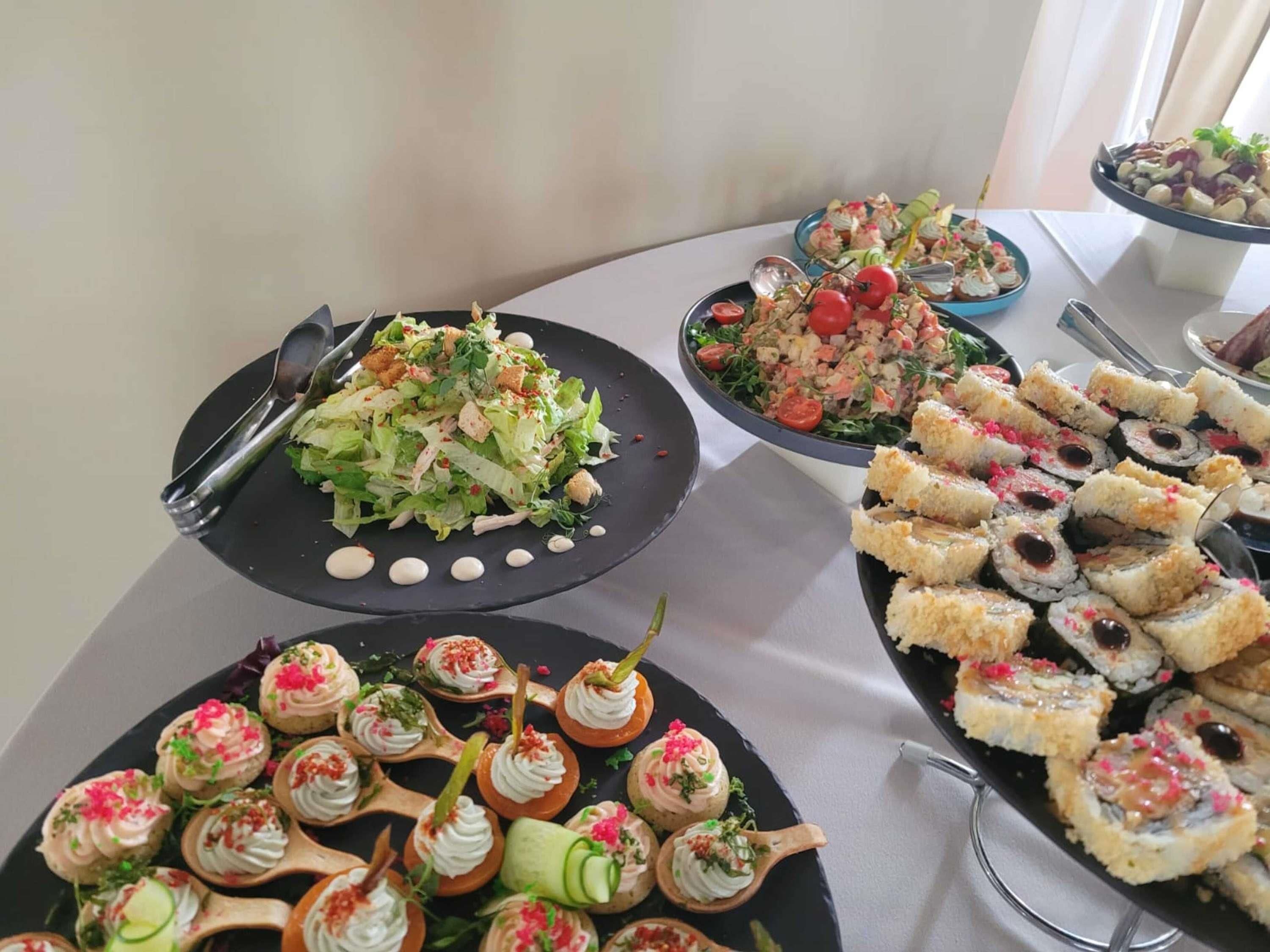 Mesa de buffet com diversos pratos, incluindo saladas, sushi e aperitivos.
