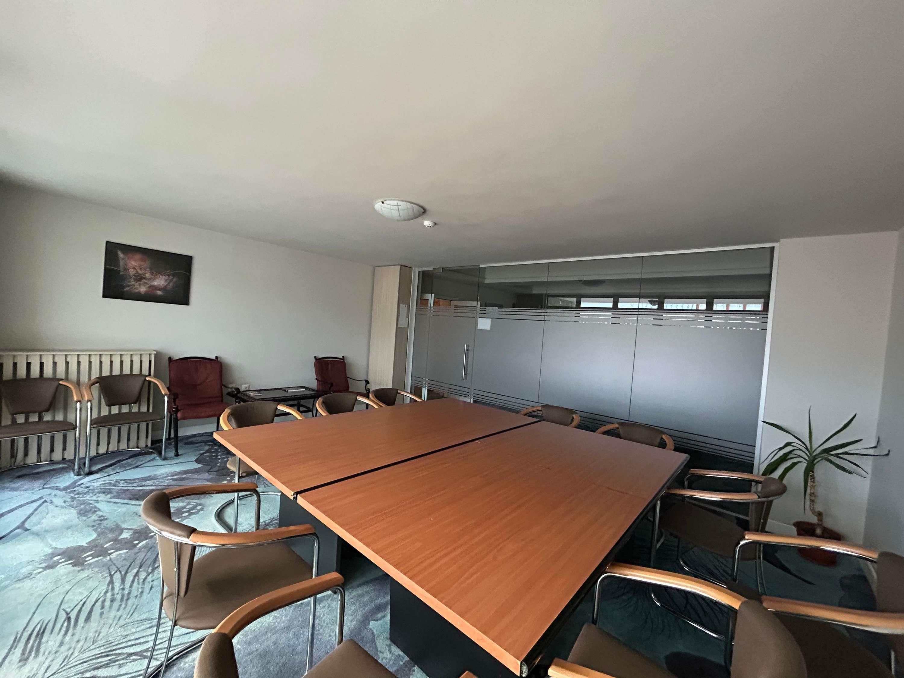 Un salón de conferencias con una larga mesa y sillas, un radiador, un cuadro y una planta en maceta.