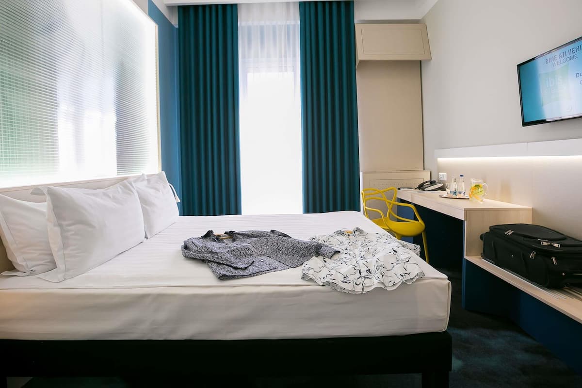 Ein Hotelzimmer mit Bett, Schreibtisch, Stuhl, Fernseher und Koffer.