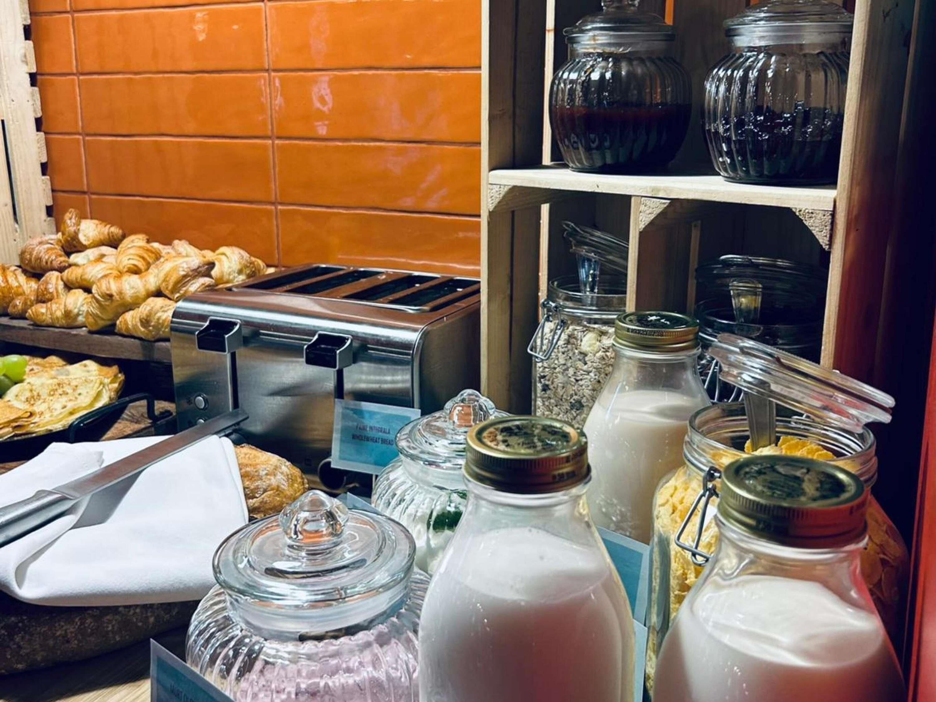 Un bufé de desayuno con bollería, una tostadora y dispensadores de leche.