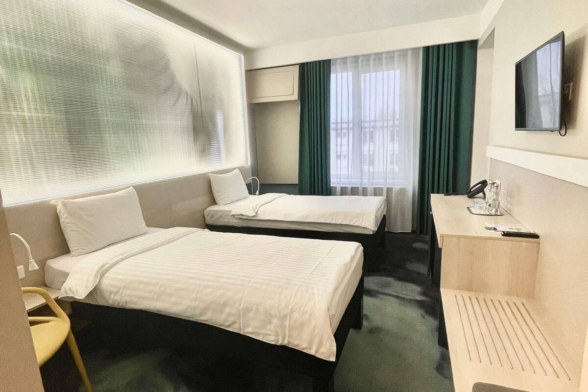 Ein Hotelzimmer mit zwei Betten, einem Schreibtisch, einem Stuhl, einem Fernseher und einem Fenster mit Vorhängen.