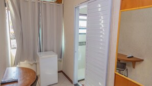 A compact room with a refrigerator, a small table, a shower area, and a sliding door leading to a balcony. - Pousada Ondas do Forte (Cabo Frio)