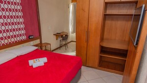 A hotel room with a red bed, wooden wardrobe, and a small desk with a chair. - Pousada Ondas do Forte (Cabo Frio)