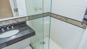 A bathroom with a glass shower enclosure, a sink with a black countertop, and tiled walls with a decorative border. - Pousada Ondas do Forte (Cabo Frio)