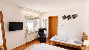 A bedroom with two beds, a TV, a chair, and a window. - Apartment Hope Inn (Gross-Zimmern)