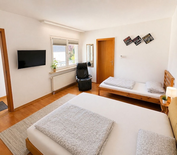 A bedroom with two beds, a TV, a chair, and a window.