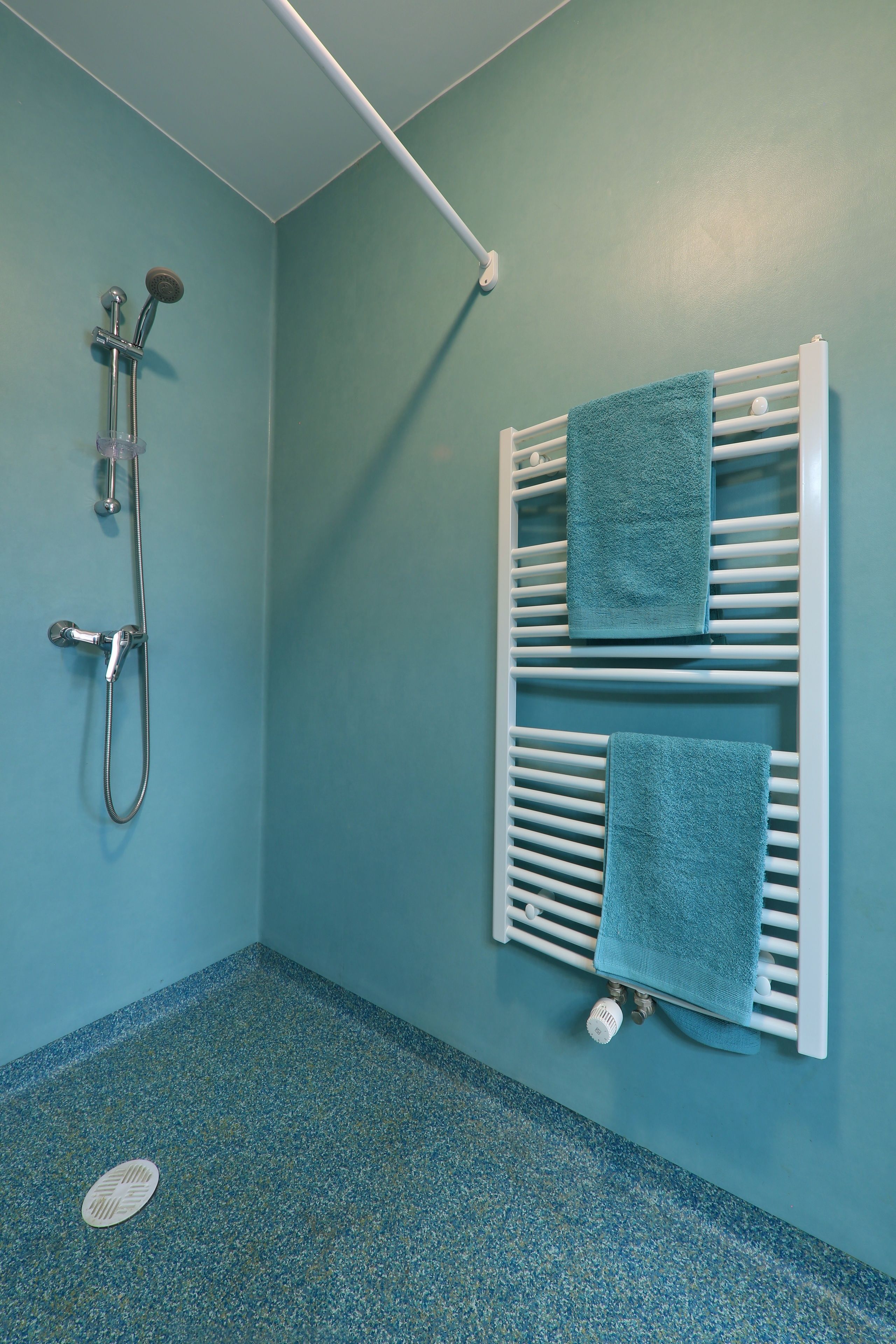 Een badkamer met een douche, een handdoekrek met twee handdoeken en een vloerafvoer.