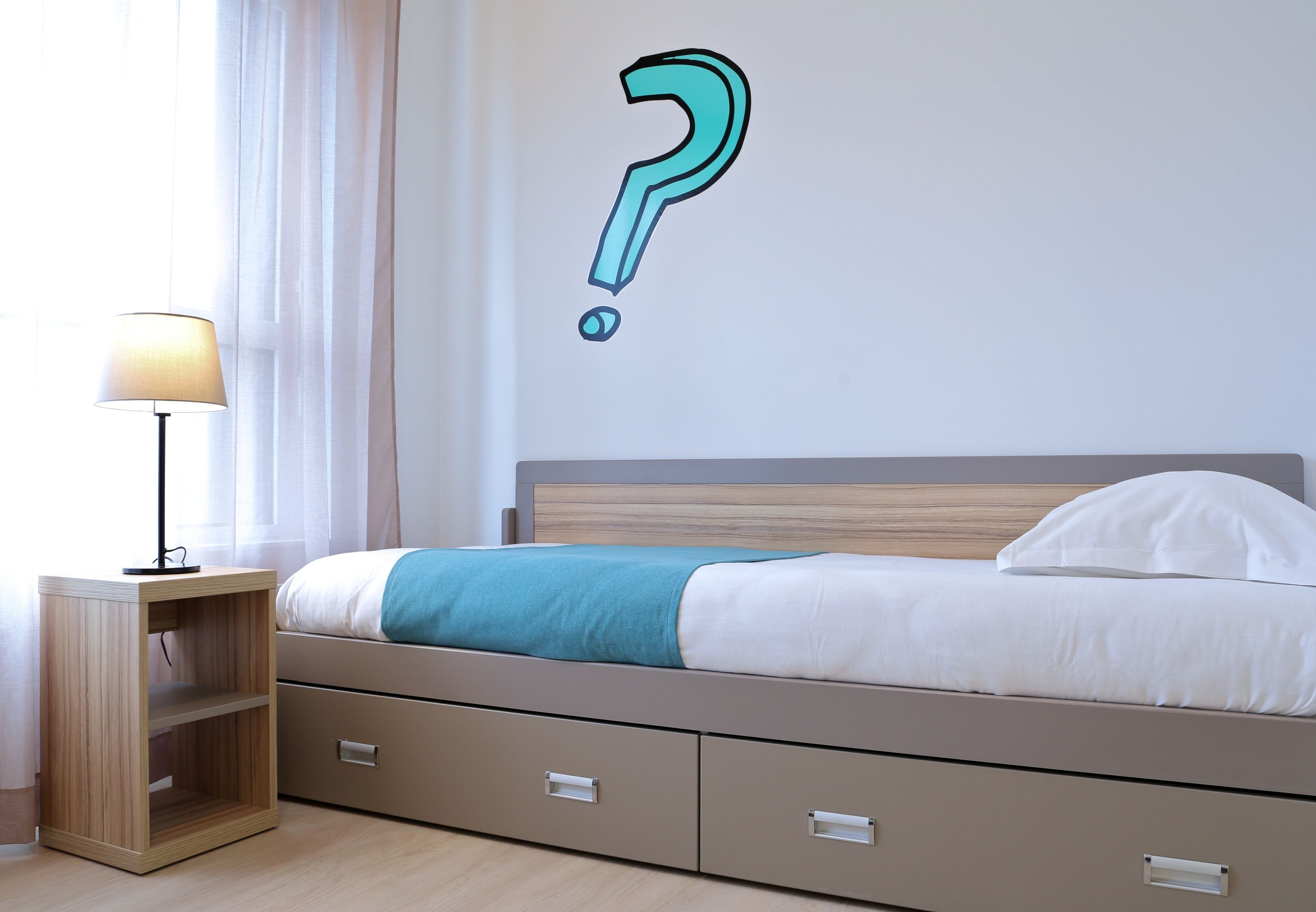 Un dormitorio con una cama, una mesita de noche y un signo de interrogación en la pared.