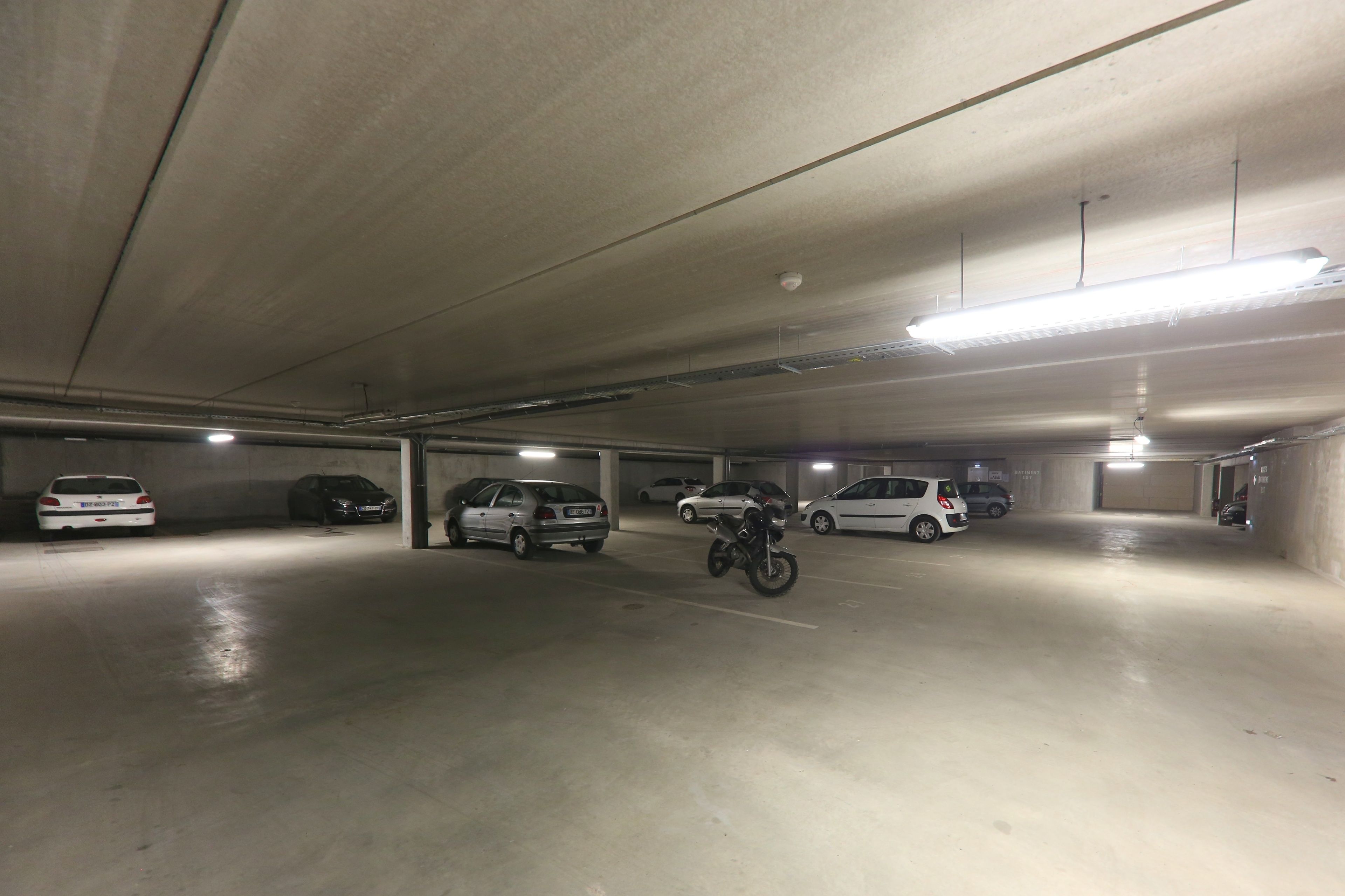 Un parking à plusieurs niveaux où sont garées plusieurs voitures et une moto.