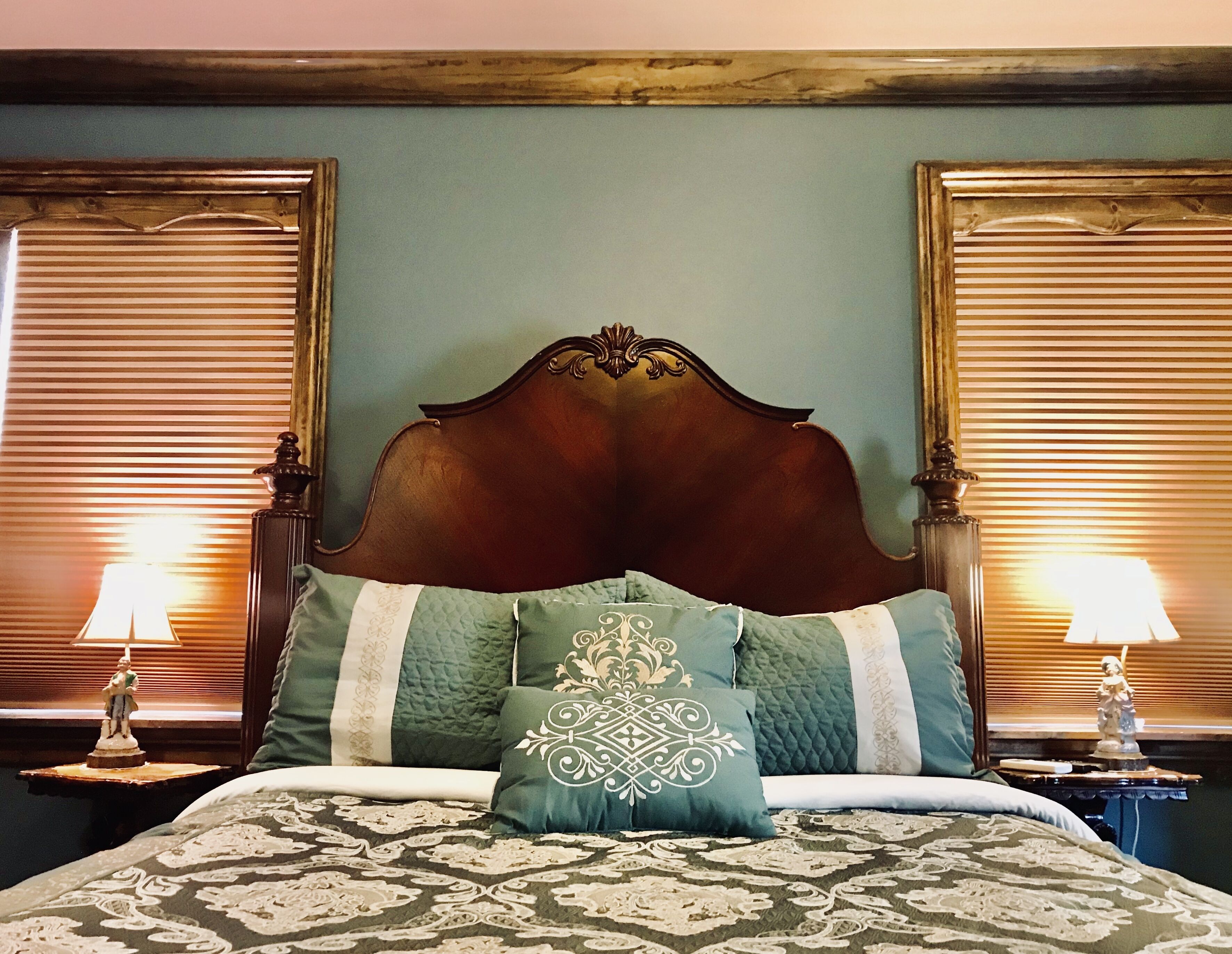 A bed with a wooden headboard, two nightstands with lamps, and a green wall.