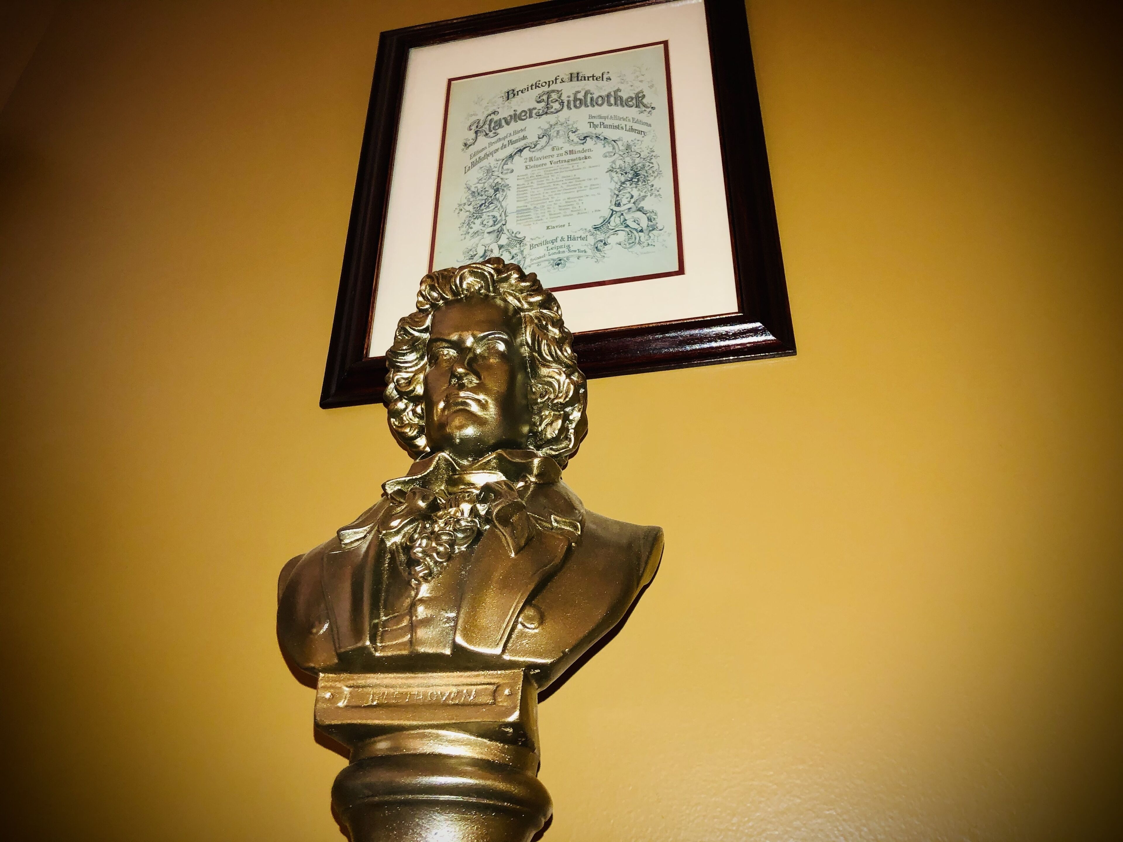 A bust of a historical figure with a plaque reading "L. Beethoven" against a yellow wall.