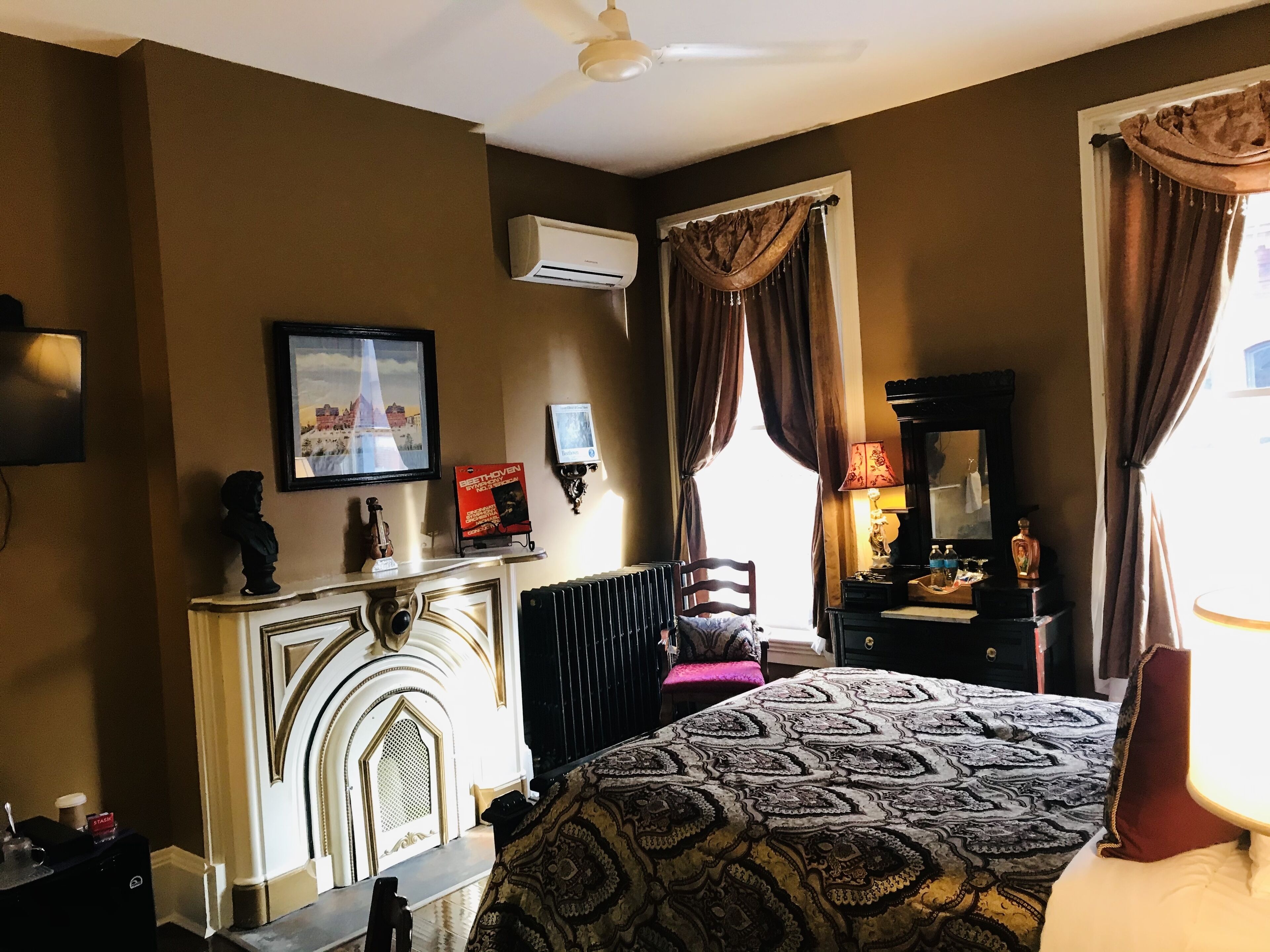 Een hotelkamer met een open haard, een bed met beddengoed met een patroon, een bureau met een lamp en een raam met gordijnen.