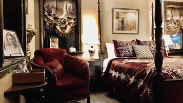 Um quarto com uma cama de dossel, uma poltrona vermelha, uma mesa de cabeceira e um quadro na parede.