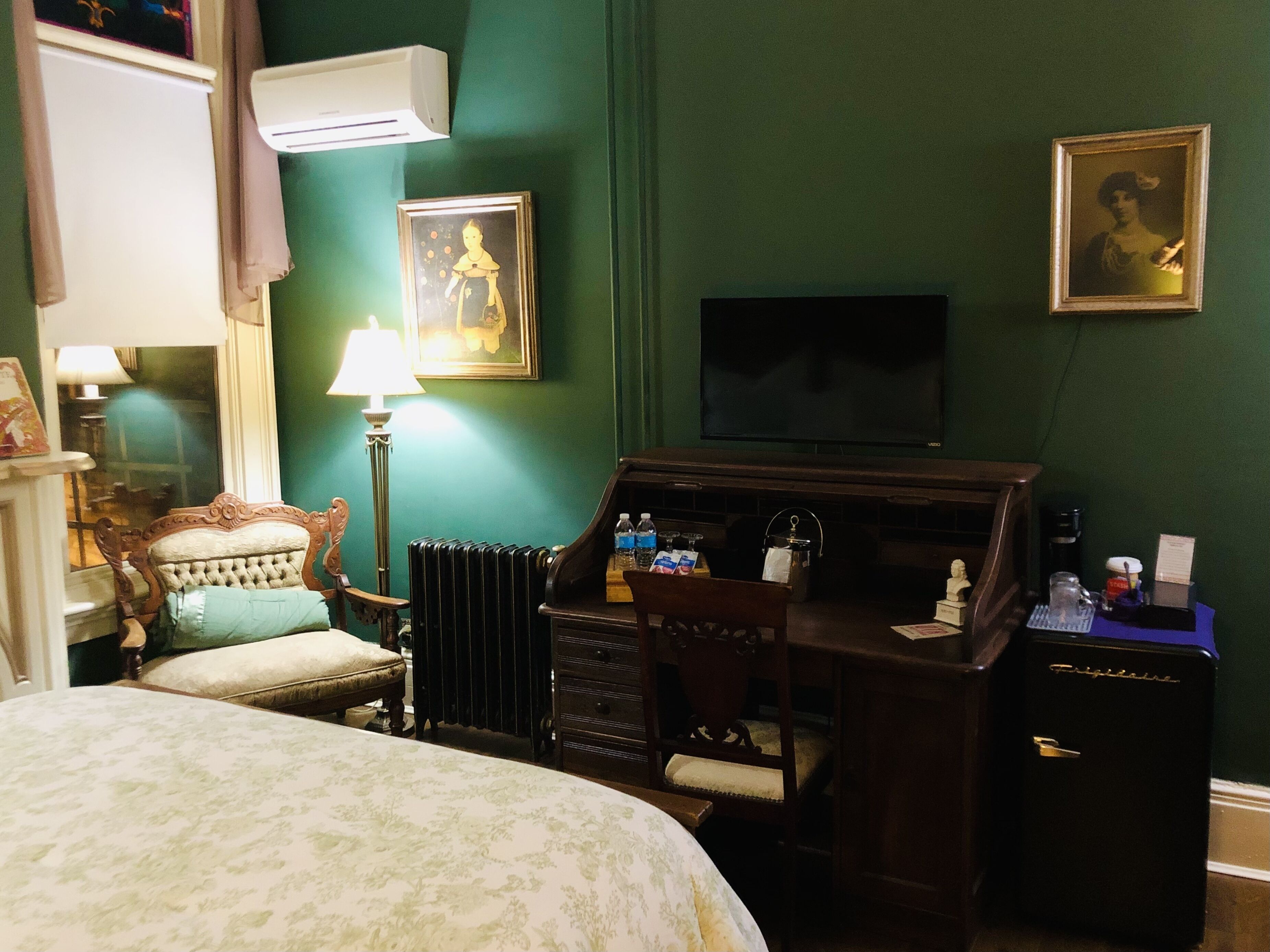 A hotel room with a bed, a desk with a computer, a radiator, a lamp, and a television.