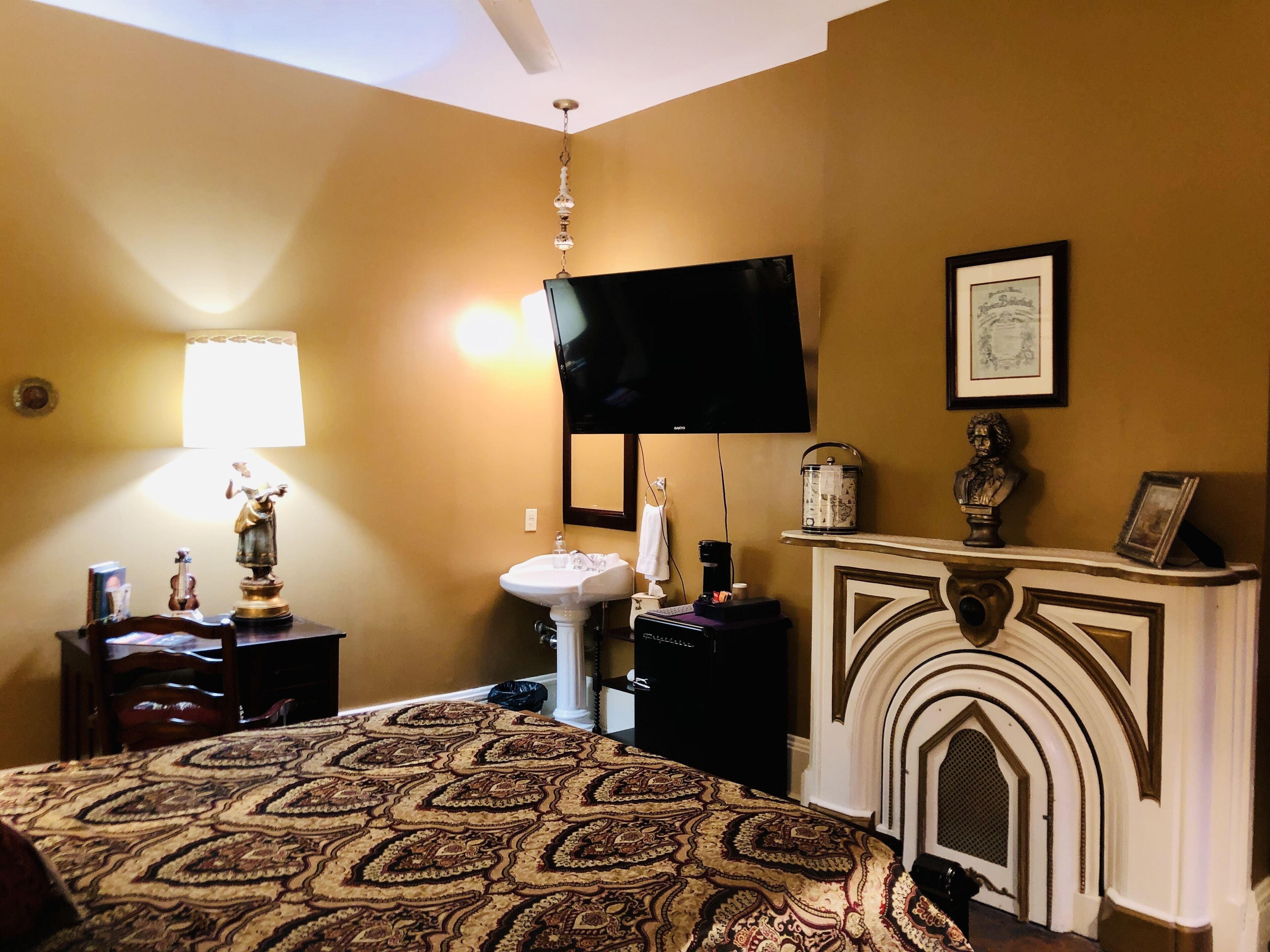 A hotel room with a bed, a television, a fireplace, a sink, and a lamp.