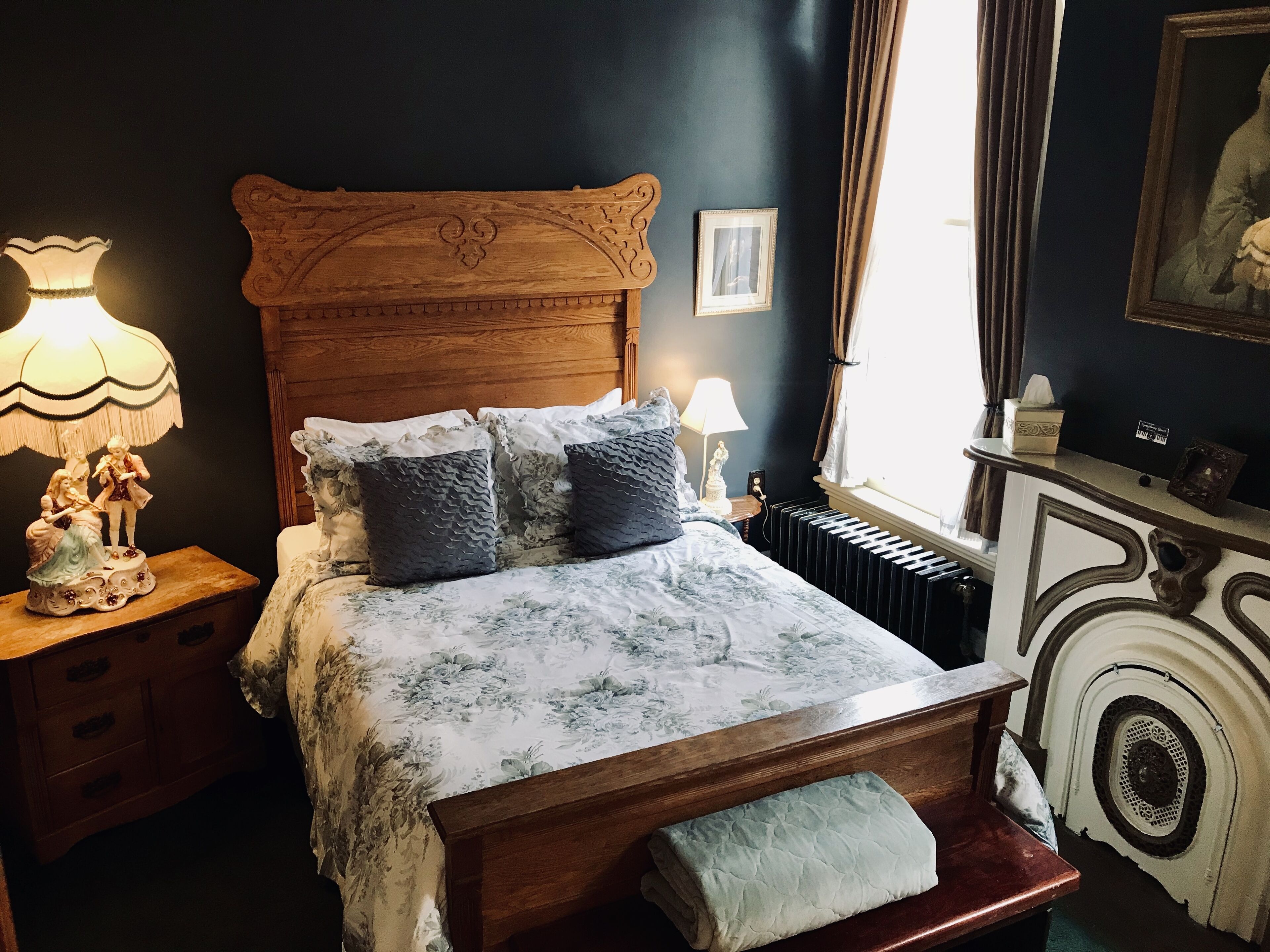 Un dormitorio con cama de madera, ropa de cama floral, una mesita de noche con lámpara y un aparador con espejo.