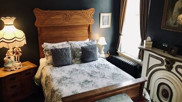 Un dormitorio con cama de madera, ropa de cama floral, una mesita de noche con lámpara y un aparador con espejo.
