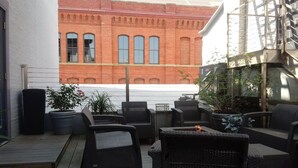 An outdoor patio with wicker furniture, potted plants, and a view of a red brick building.