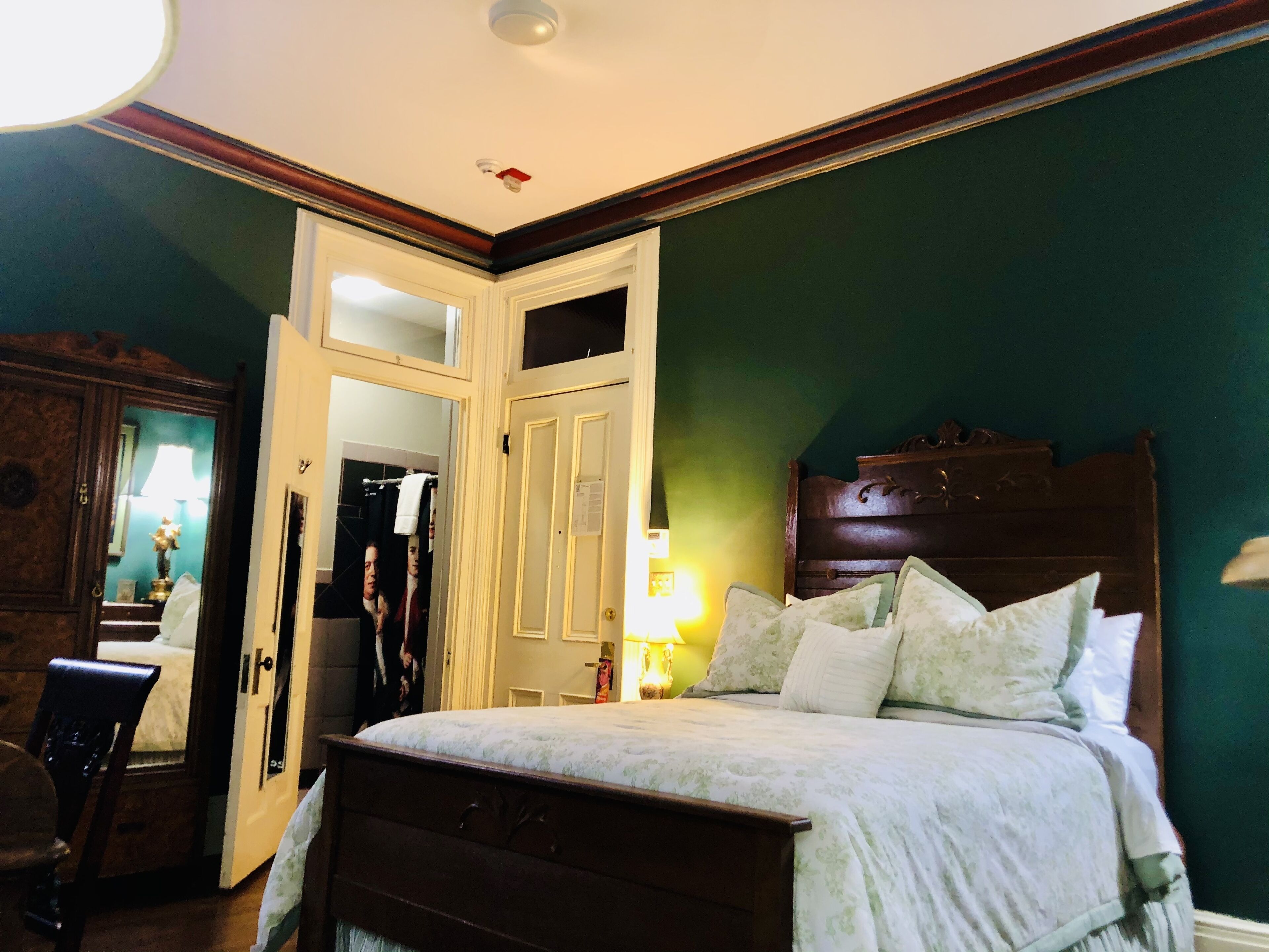 A bedroom with a bed, a nightstand, a lamp, a mirror, and a wardrobe.