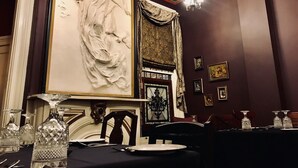 A dining area with a table set for two, a chandelier, and a large wall sculpture.