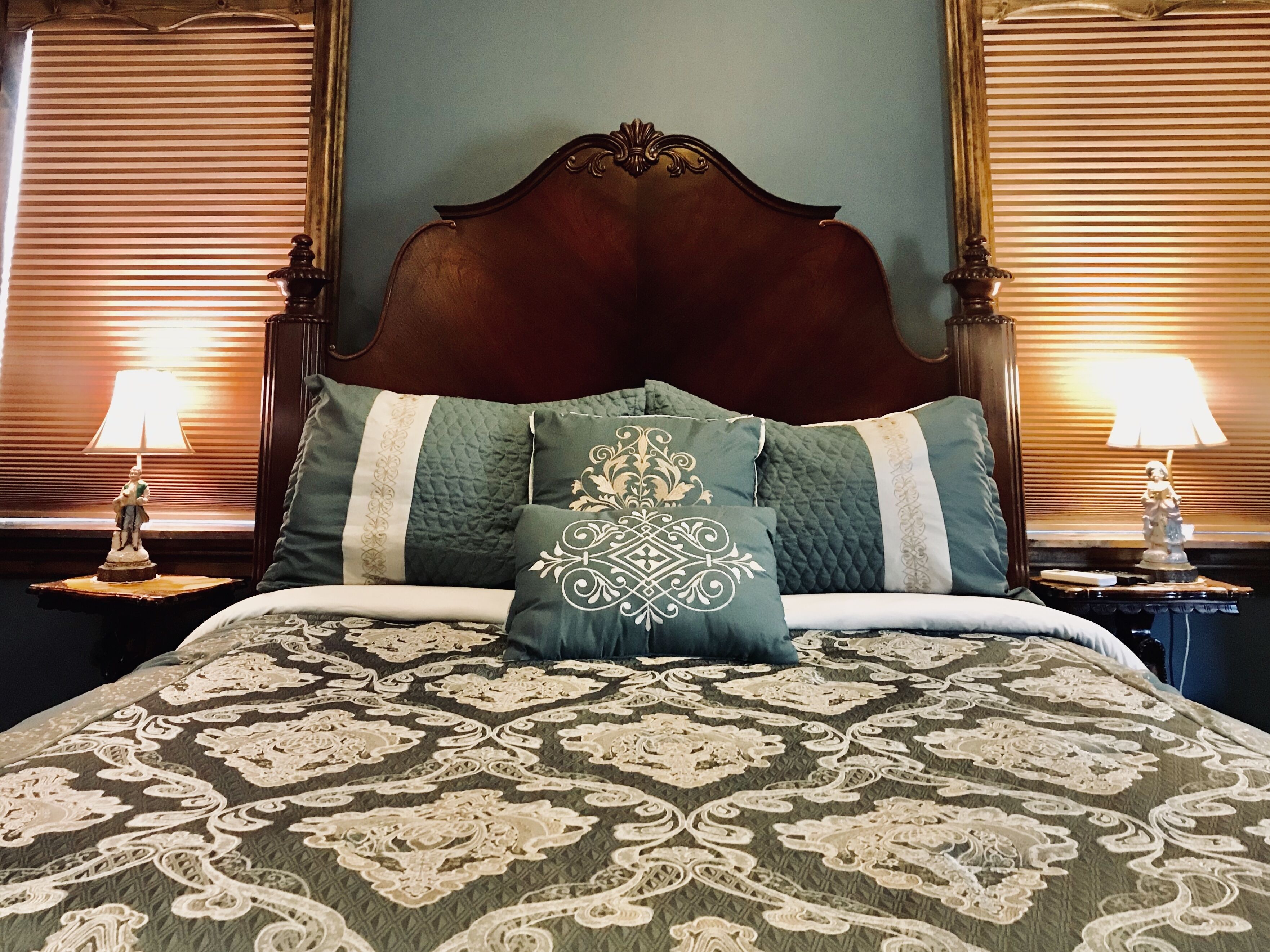 Una cama con cabecera oscura, almohadas verdes y blancas, y una colcha estampada.