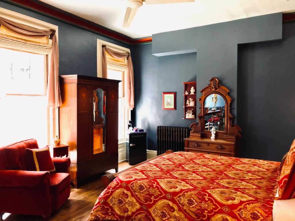 A bedroom with a large bed, a wooden dresser, a red armchair, and a radiator.