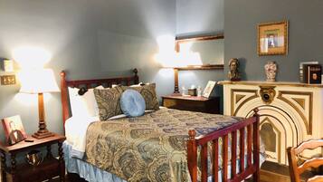 A bedroom with a wooden bed, a nightstand with a lamp, a dresser, and a fireplace.