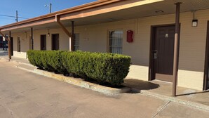 Un motel doté d’un parking couvert, d’une rangée de chambres et d’une haie bien entretenue le long du trottoir.