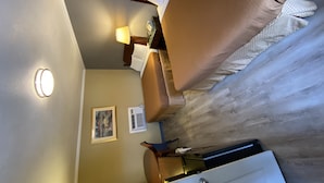 Une chambre d’hôtel avec un lit, une table de chevet, une lampe, un tableau encadré au mur et une fenêtre.