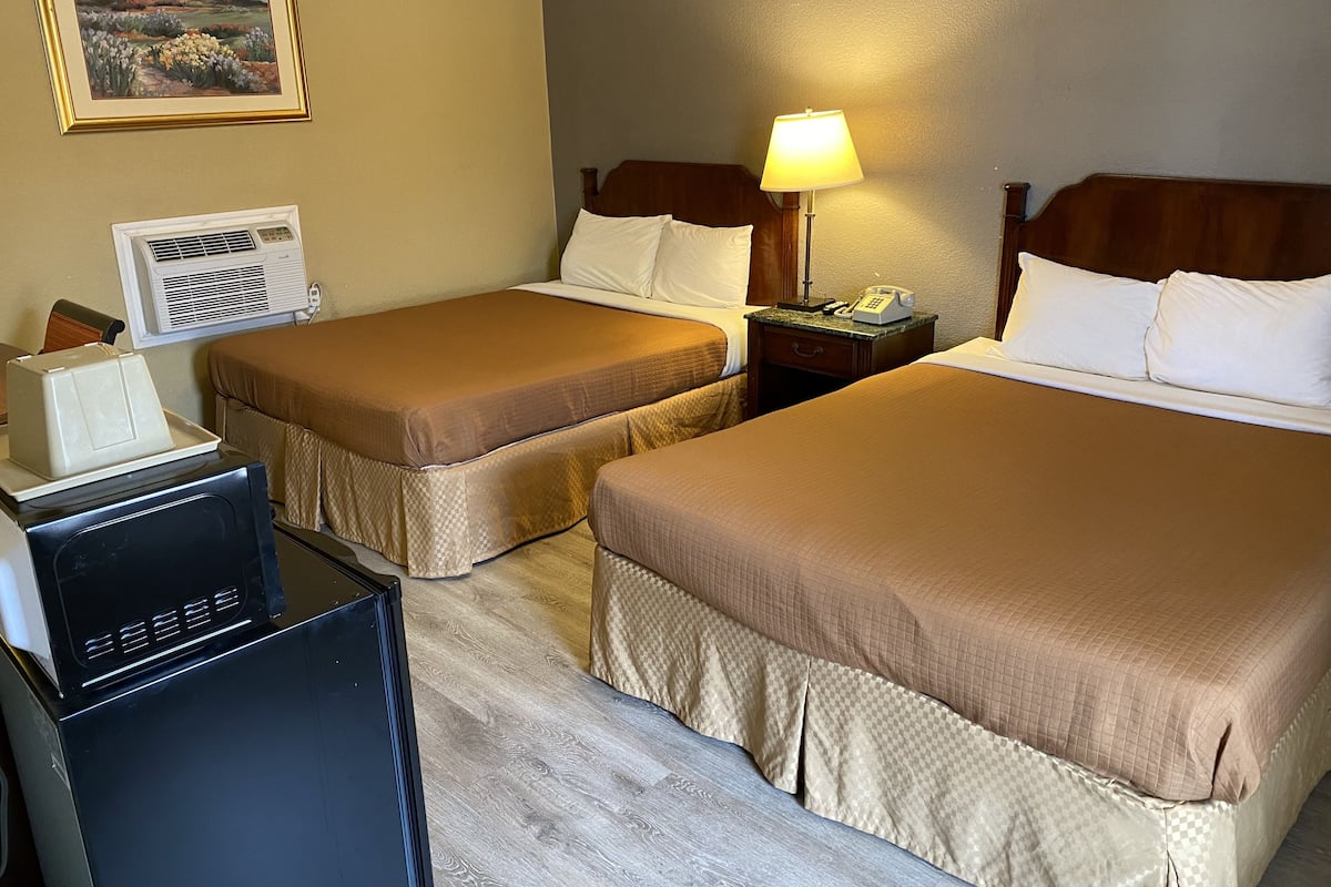 A hotel room with two beds, a desk with a computer, a lamp, and a painting on the wall.