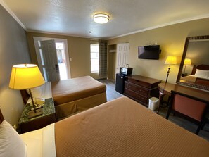 Habitación de hotel con dos camas, un escritorio, una cómoda, un televisor y la puerta del baño.