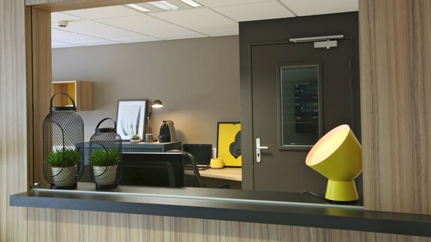 A modern office space with a desk, computer, and decorative items including two potted plants and a yellow lamp. - Apparteo Dijon (Dijon)
