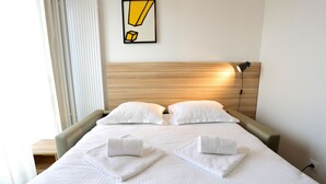 A neatly made bed with white linens and two towels folded at the foot. - Apparteo Dijon (Dijon)