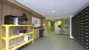 A reception area with a wooden wall, a yellow shelving unit with books, a desk with a lamp, and a wall-mounted bike rack. - Apparteo Dijon (Dijon)
