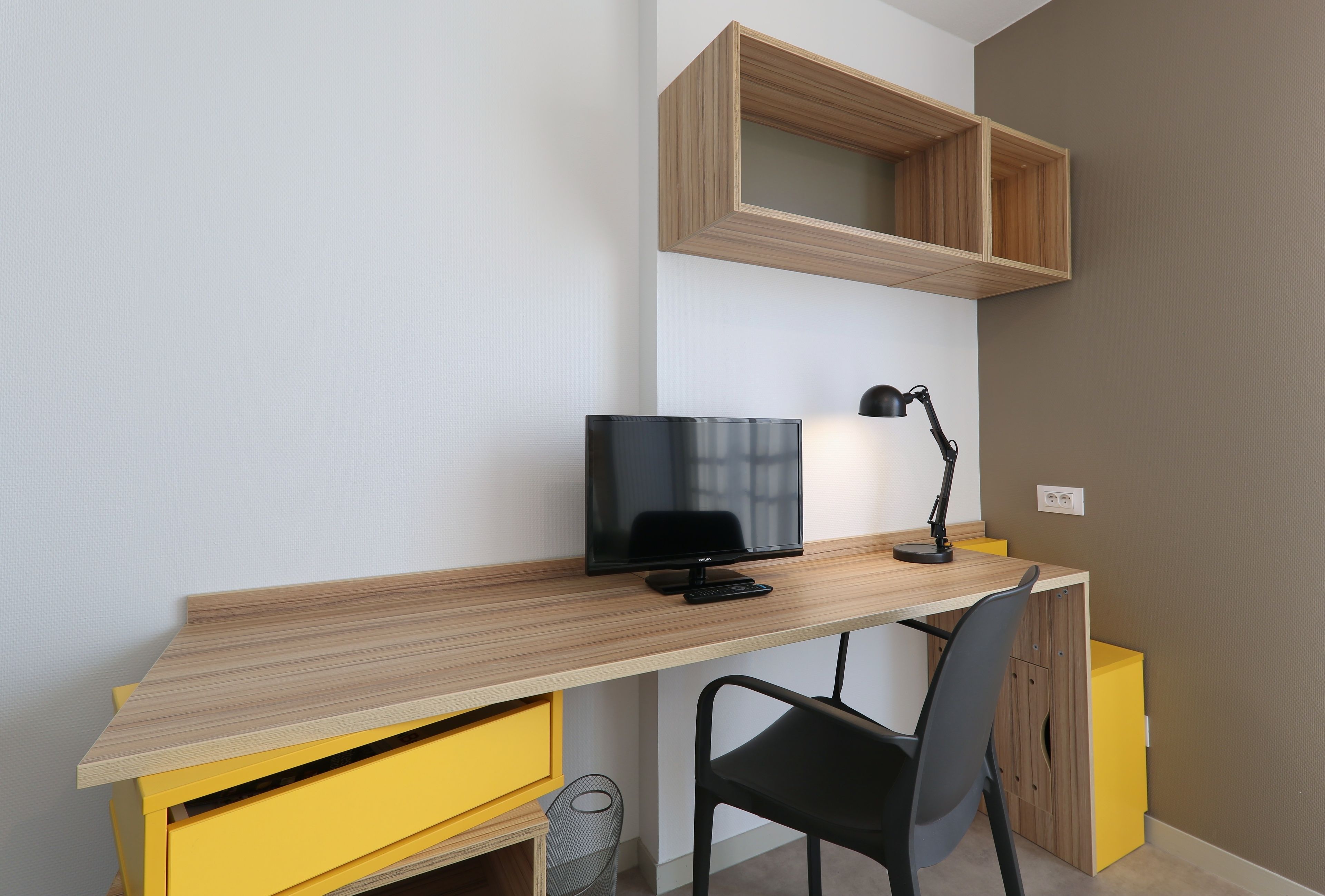 A modern workspace with a wooden desk, a black chair, a television, and a desk lamp.