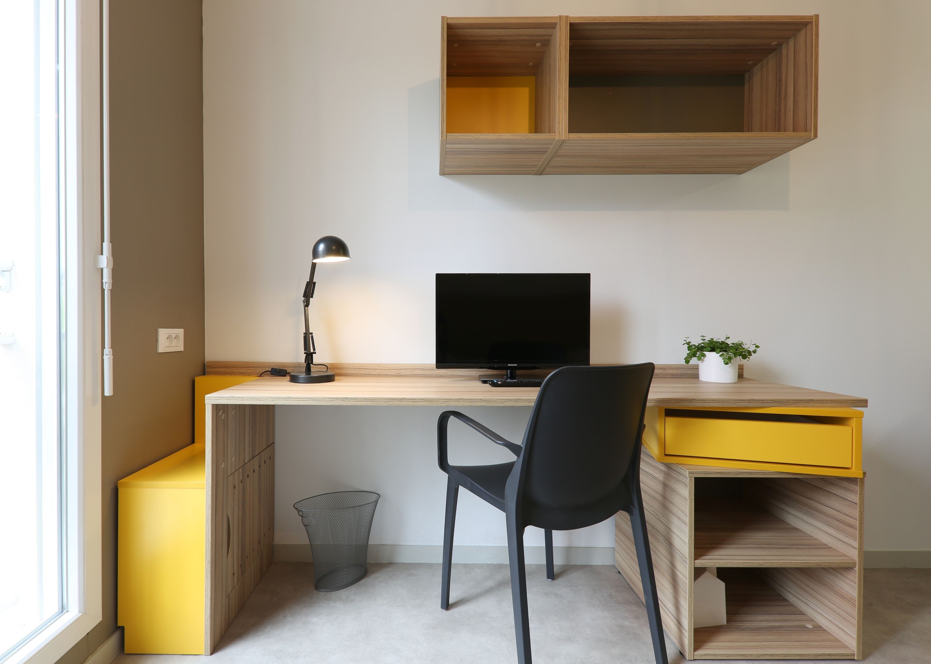 Un espacio de trabajo moderno con escritorio, ordenador, silla, lámpara y estanterías.