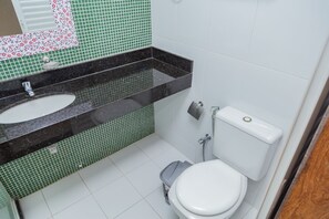 Een badkamer met een wit toilet, een wastafel met een zwart aanrechtblad en groene betegelde muren.