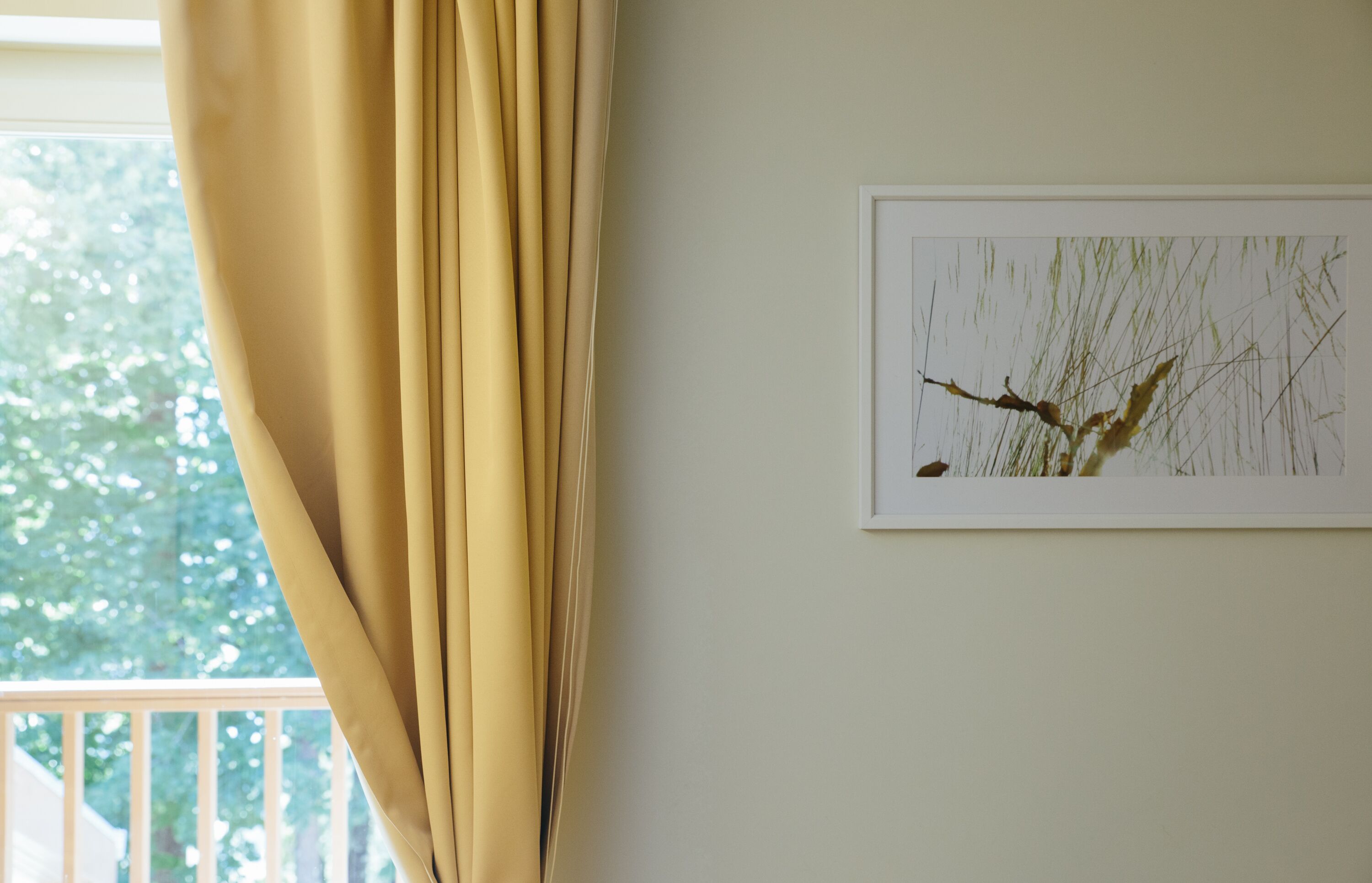 Una habitación con ventana, cortina y un cuadro en la pared.