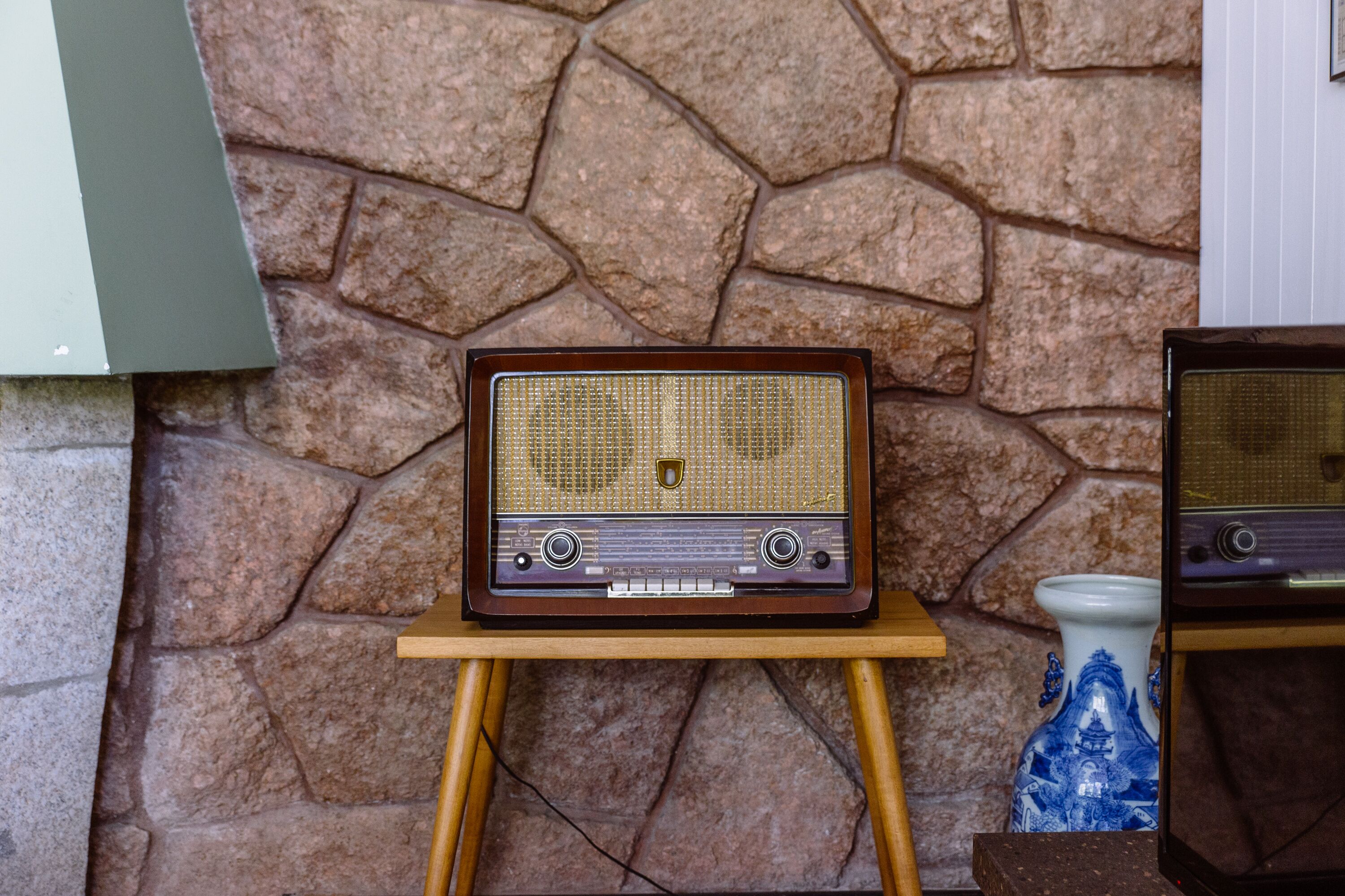 A vintage radio on a wooden stand against a stone wall.