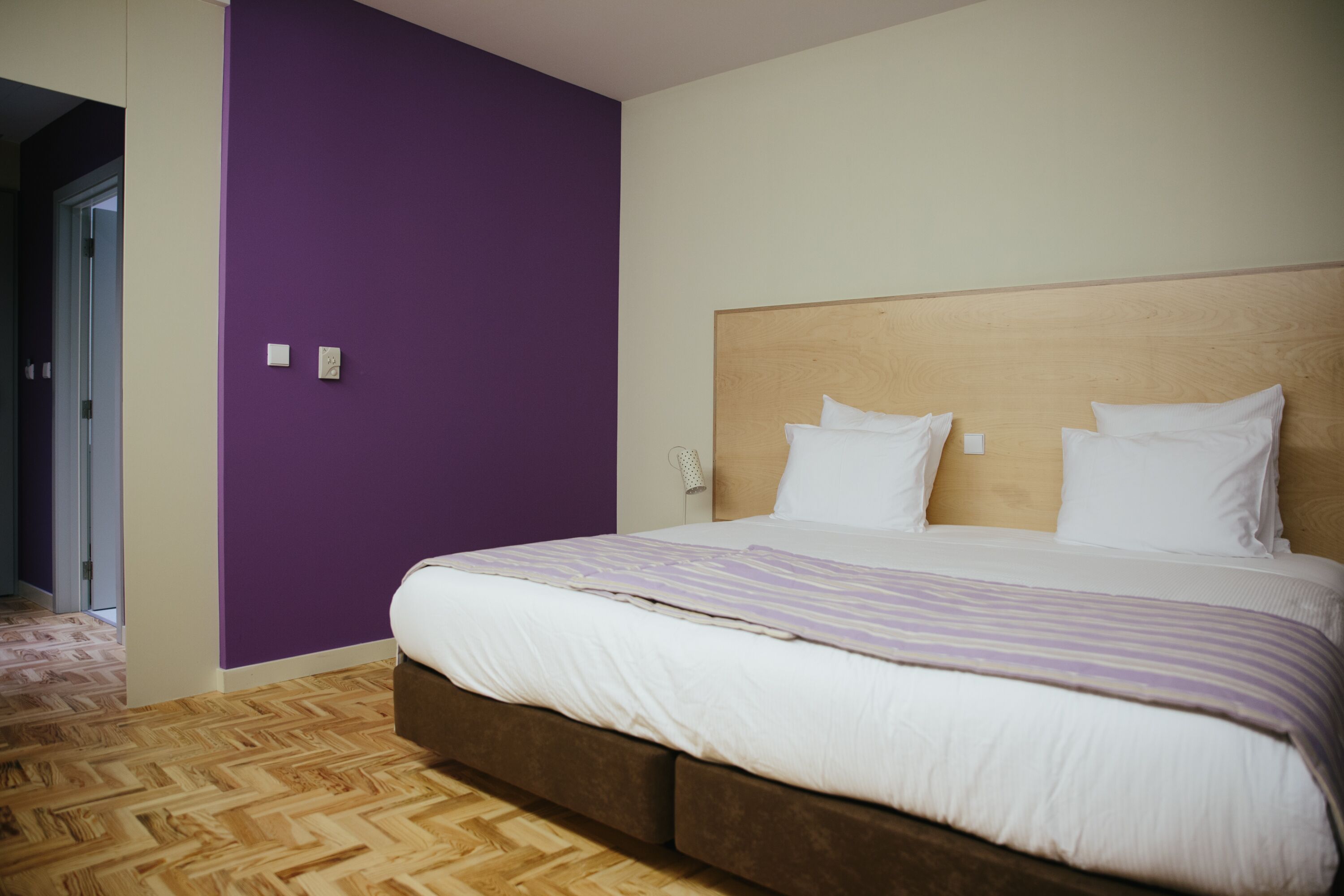 Ein Hotelzimmer mit Bett, einem Holz-Kopfteil und einer violetten Wand.