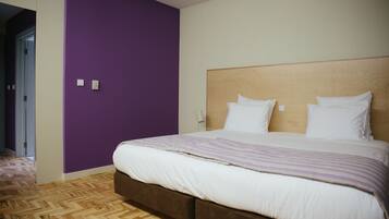 A hotel room with a bed, a wooden headboard, and a purple wall.
