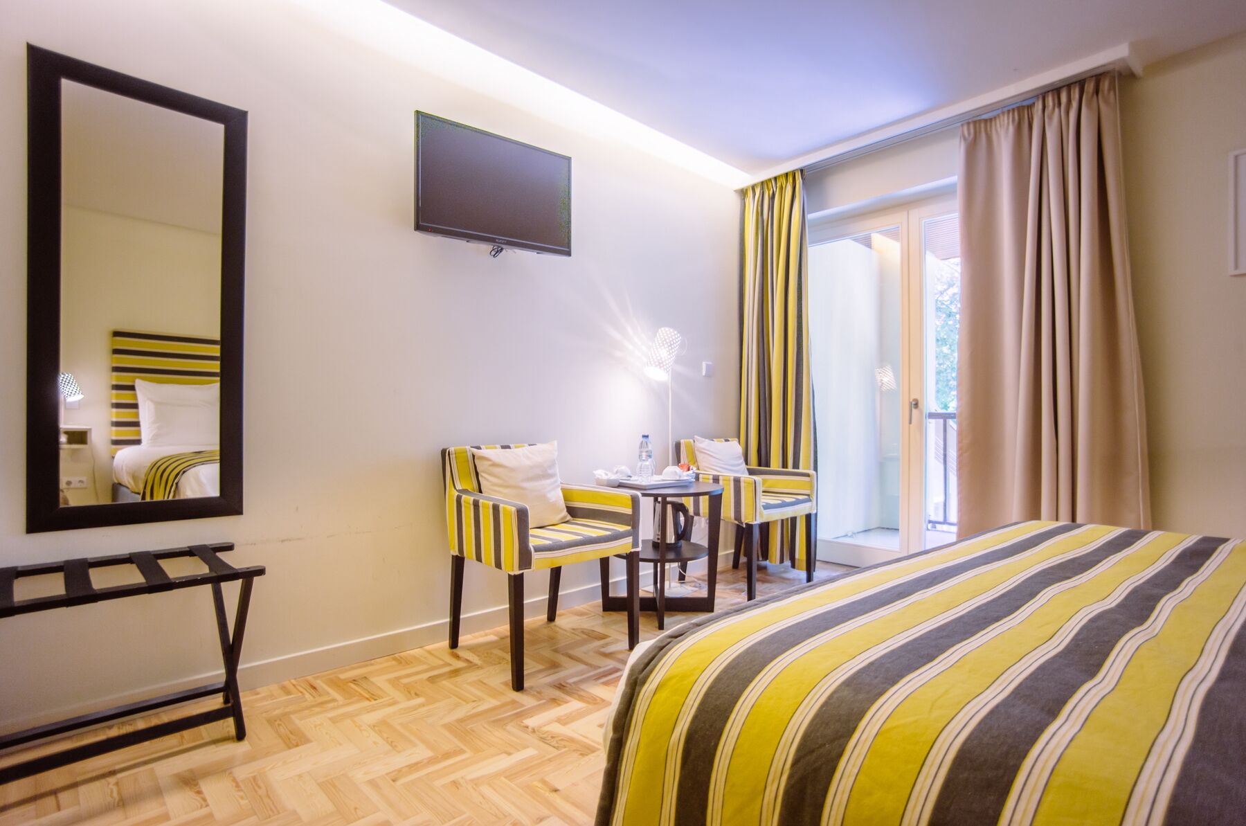 A hotel room with a bed, a desk with two chairs, a flat-screen TV, and a sliding glass door to the outside.