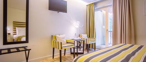 Habitación de hotel con cama, escritorio con dos sillas, televisor de pantalla plana y puerta corrediza de cristal al exterior.
