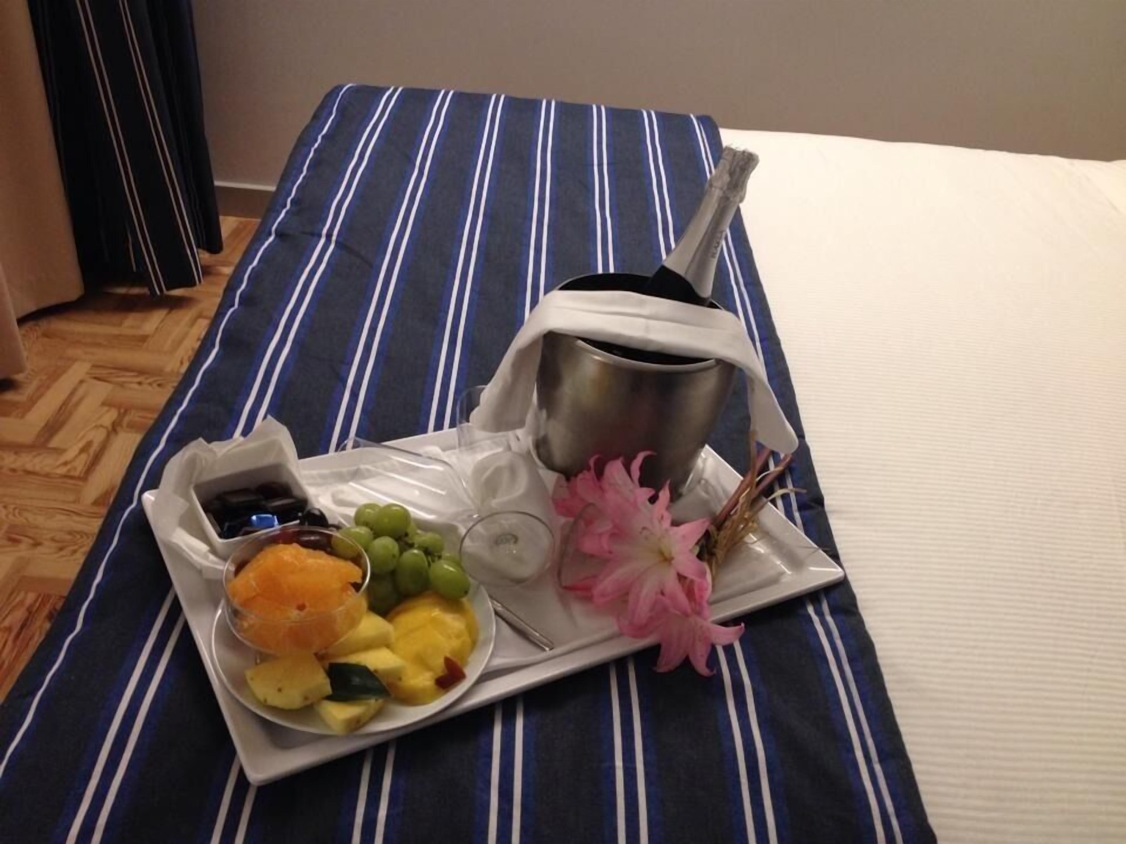 A bed with a blue and white striped bedspread, a tray with a drink, fruit, and a flower.