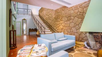Amplia sala de estar con sofá azul claro, pared decorativa de piedra, chimenea y escalera que conduce a un nivel superior.
