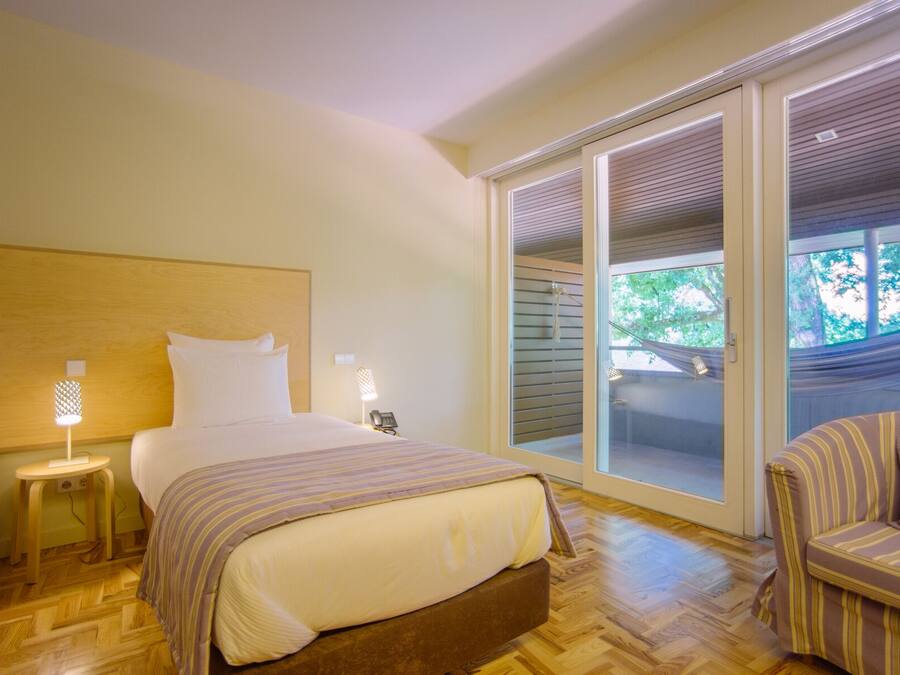 A hotel room with a bed, bedside tables, a chair, and a sliding glass door leading to a balcony.