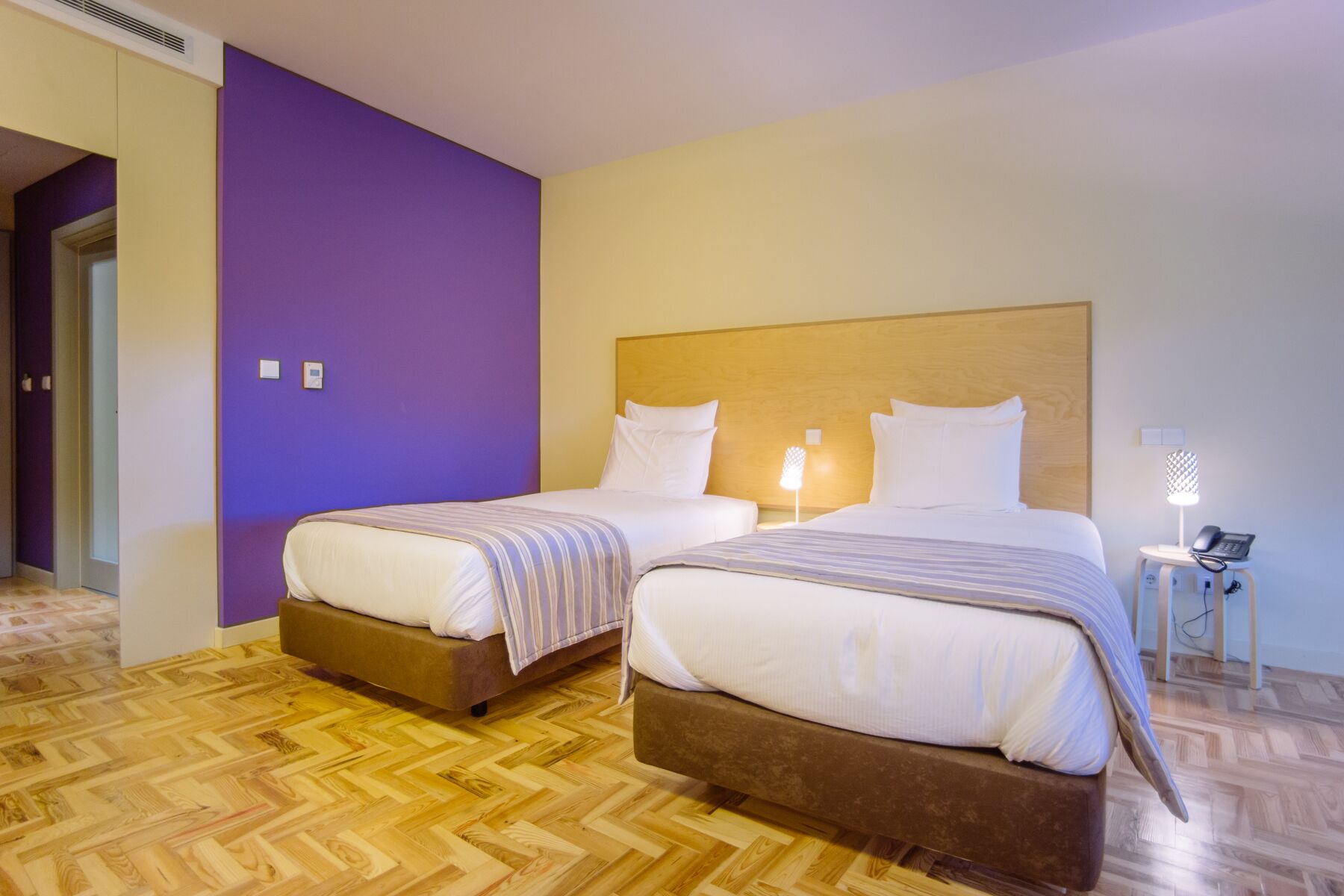 Habitación de hotel con dos camas, suelo de madera y una pared de acento morada.