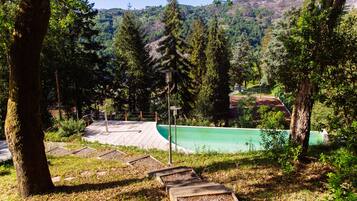 A pool area with a wooden deck, surrounded by trees and a view of a hilly landscape.