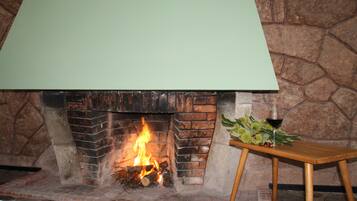 Una chimenea con un fondo de pared de piedra, una mesa con una copa de vino tinto y una planta verde.