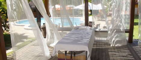Un espace extérieur abrité avec vue sur la piscine, une table de massage et une terrasse en bois.